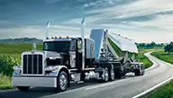 Black and chrome Peterbilt Model 389X driving on a winding road set against beautiful green pastures - Thumbnail
